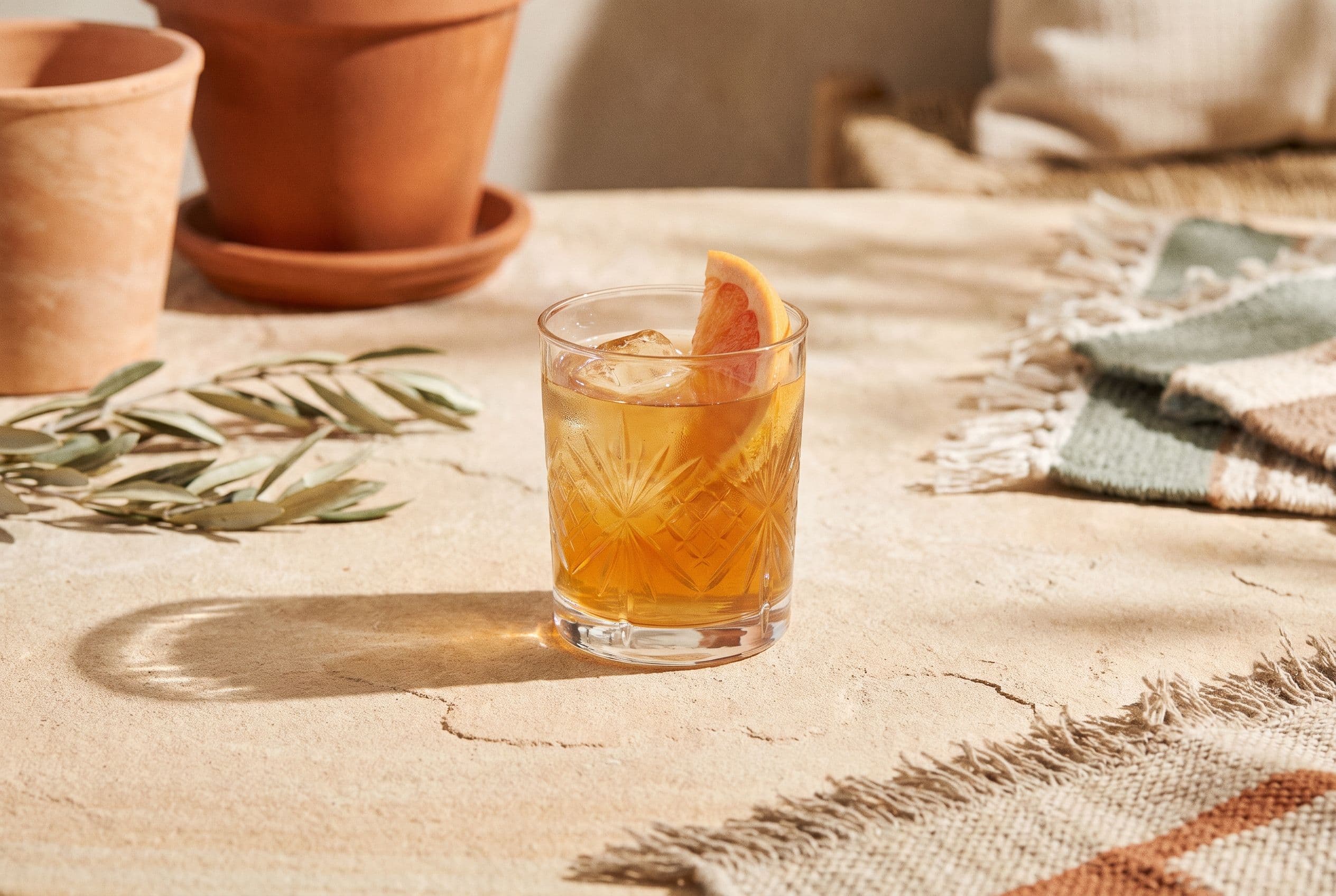 Amber botanical spritz with citrus twist in a cut-glass tumbler on a stone table